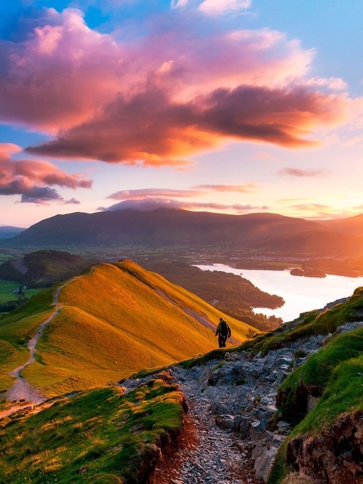 Hiker walking along a path on the mountain ridge at sunset