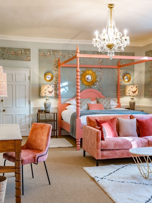 An interior shot of a colourful hotel room featuring a pink four poster bed