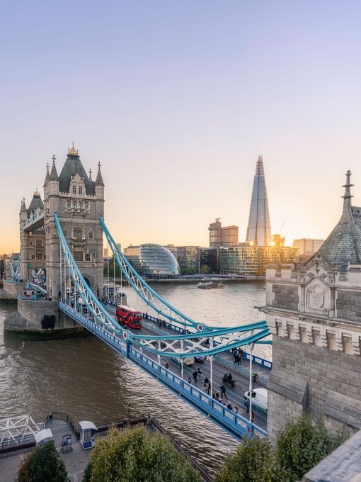 View of Tower Bridge and Shard at sunset, with a red bus going across the bridge.