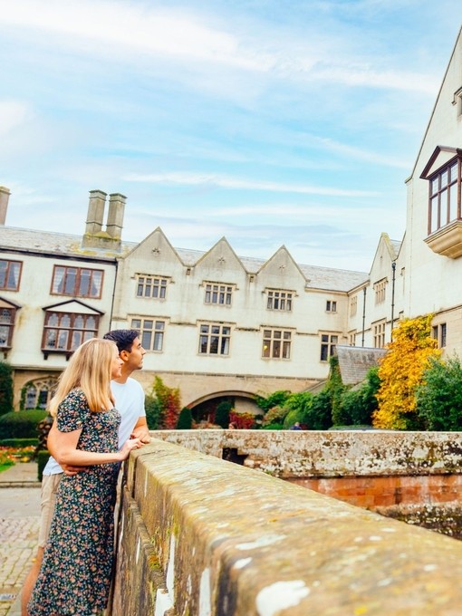 Young couple stood on stone bridge looking at country house