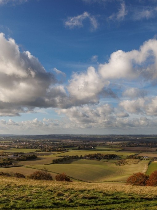 Panoramic view or rolling green farmland and pastures with a cloudy sky.