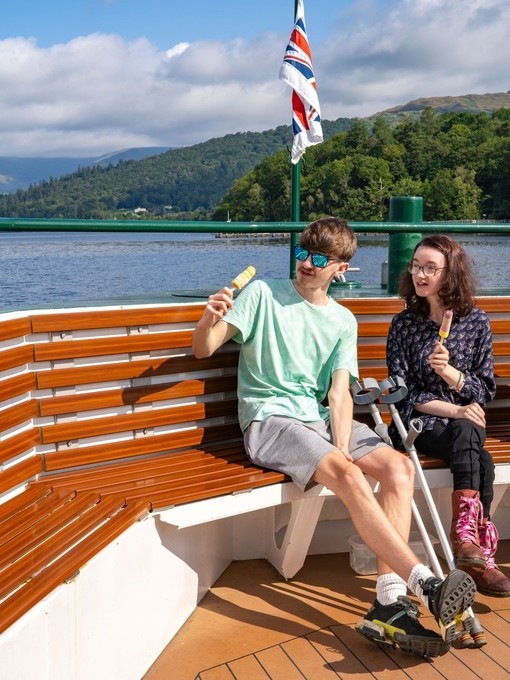 Three people sit at the end of a boat on a lake eating ice creams