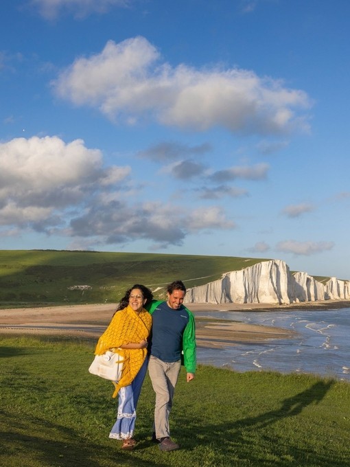 A woman and a man walk together on a headland with chalk cliffs beyond
