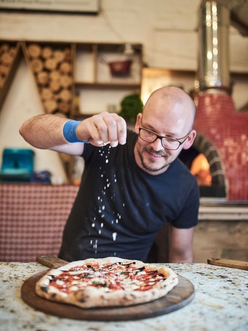 Man sitting at table, sprinkling cheese on pizza