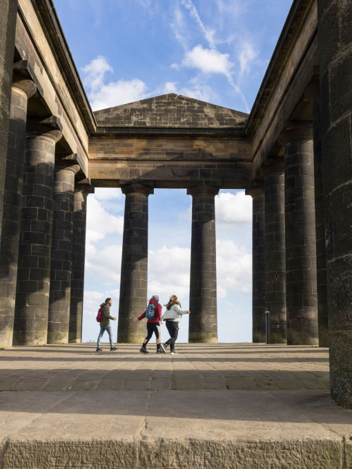 Three people exploring an antique stone monument with large archways and pillars.