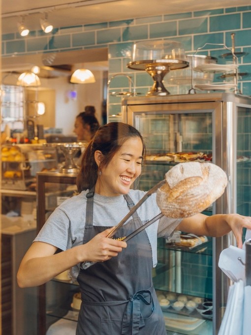 Smiling woman lifting loaf of bread with tongs