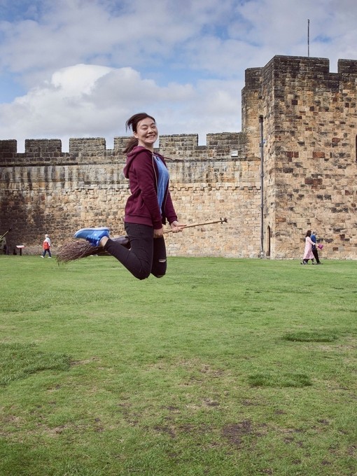 Young woman hovering on a broomstick in the Outer Bailey of Alnwick Castle