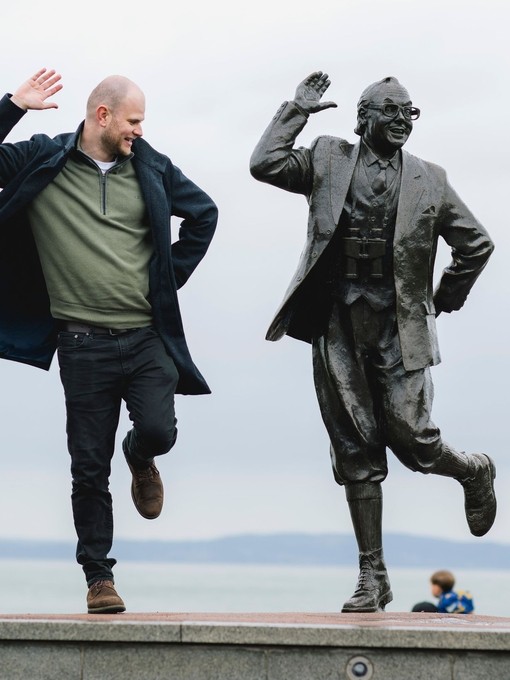 Man, toddler and statue of a man in front of the sea
