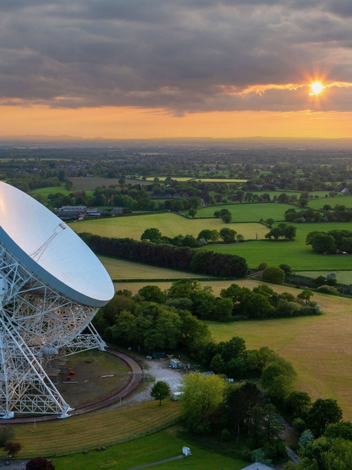 View of a large radio telescope surrounded by green fields and trees in the countryside 