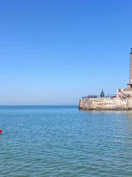 A man standing on a paddle board in a city harbour by a stone pier.