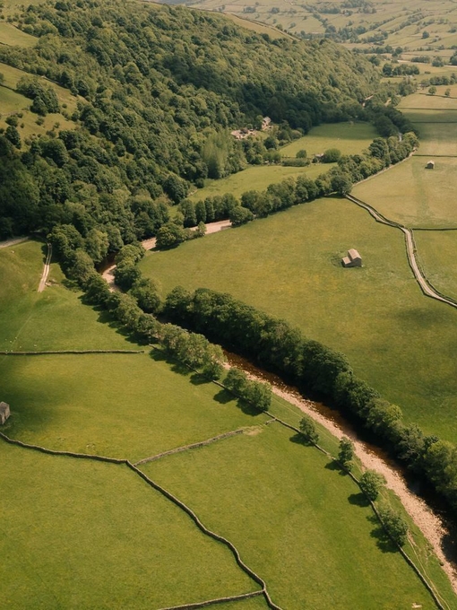 An aerial view of a river surrounded by green fields, trees, and rolling hills.
