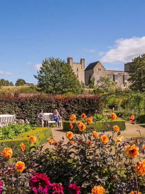 Two female friends sat on a bench in a formal garden