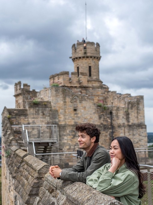 A man and a woman look out to a view from a castle