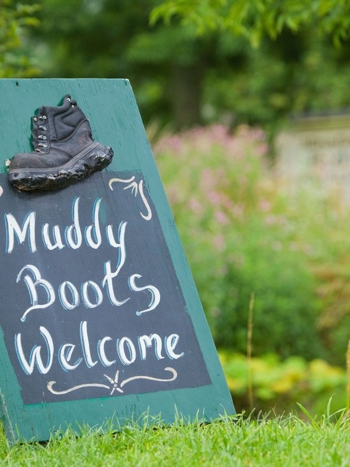 Signage on grass saying 'Muddy Boots Welcome' with plants