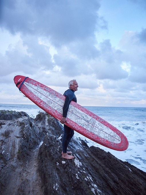 Man carrying surfboard and wearing wet suit on the rocks