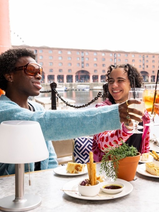 A group of friends raise a toast outside a restaurant with docks in the background