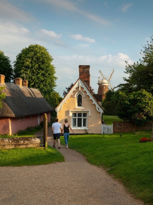 A man and a woman walk toward thatched cottage and a windmill