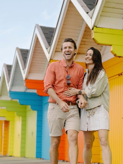 A man and woman laughing outside colourful beach huts
