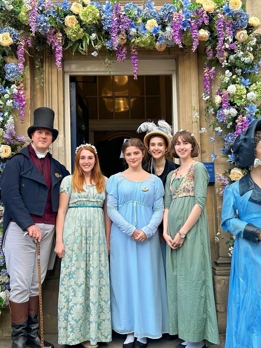 A group of people posing in period Victorian costume under a floral archway.