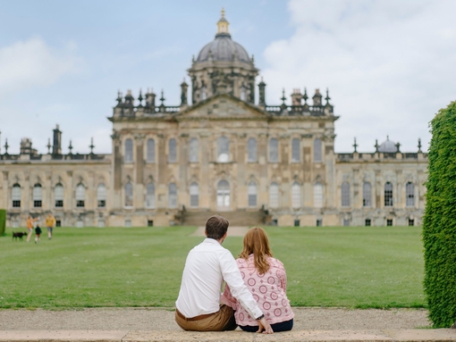 A man and a woman sit on a step looking towards a heritage building