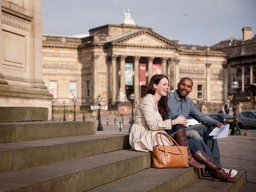 Liverpool city centre. Lime Street. Two people, a couple, sitting on the steps outside St George's Hall in front of the Walker Art Gallery, in Liverpool.