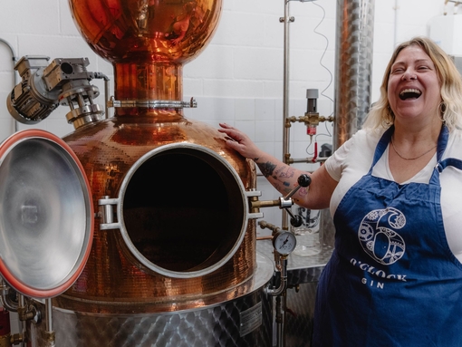 A female tour guide wears an apron and stands by a still at a distillery
