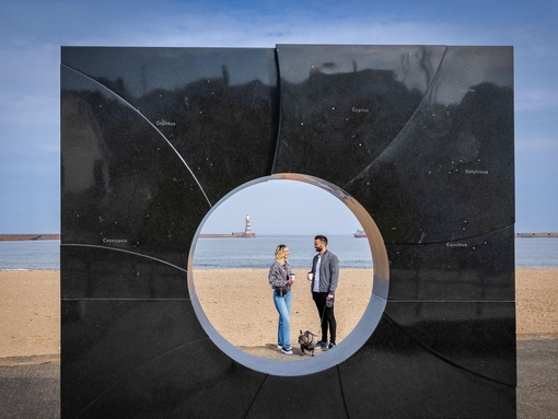 Two people seen through an art display on a beach sculpture trail.