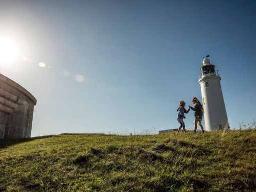 Two children playing in open space by a lighthouse