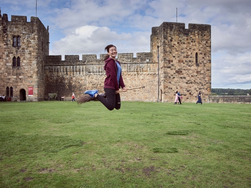 Young woman hovering on a broomstick in the Outer Bailey of Alnwick Castle