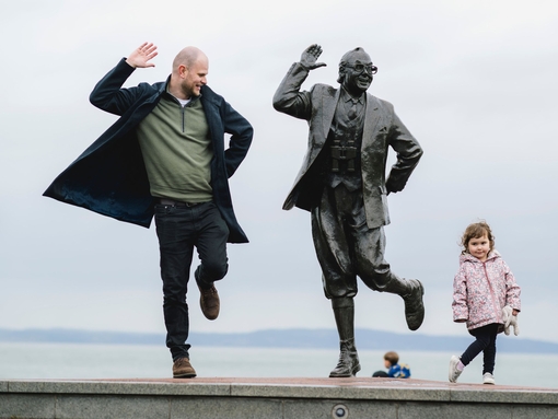 View of man, female child and statue of a man in front of the sea