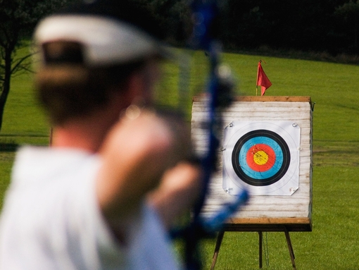 A person aiming a bow at a target from distance