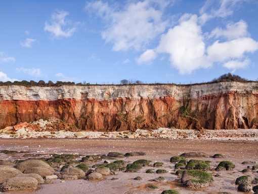 View of cliffs with white chalk overlaying red limestone in a colourful formation.