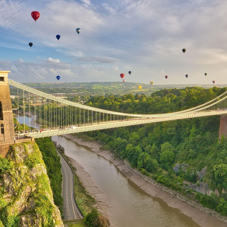 Aerial view of a large suspension bridge with hot air balloons taking to the air