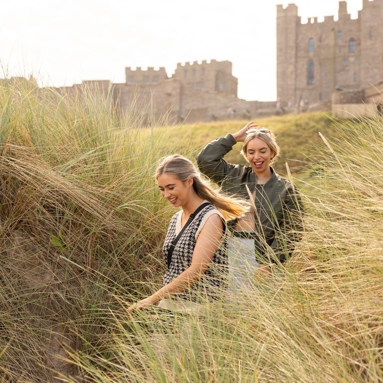 A couple walking in the sand dunes near Bamburgh Castle