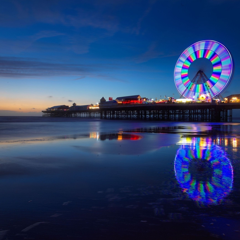 Colourful big wheel lit up on a pier at night.