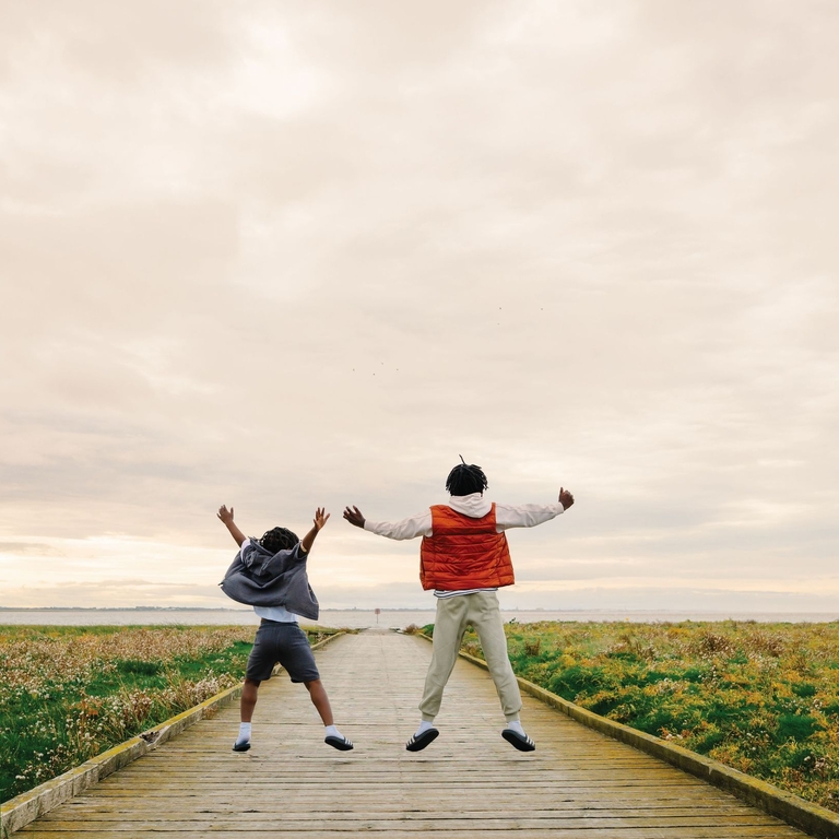 Two young boys jumping on a wooden jetty by the sea