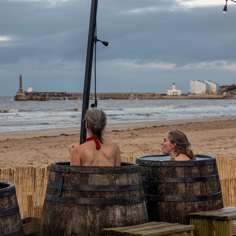 Two women in barrels in an outdoor beachside sauna.