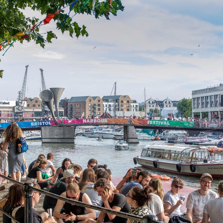 Crowds of people sitting on the harbourside in Bristol, watching ships go past