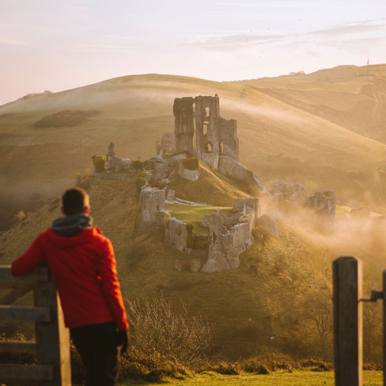 Man leaning on gatepost, looking at the ruins of a castle