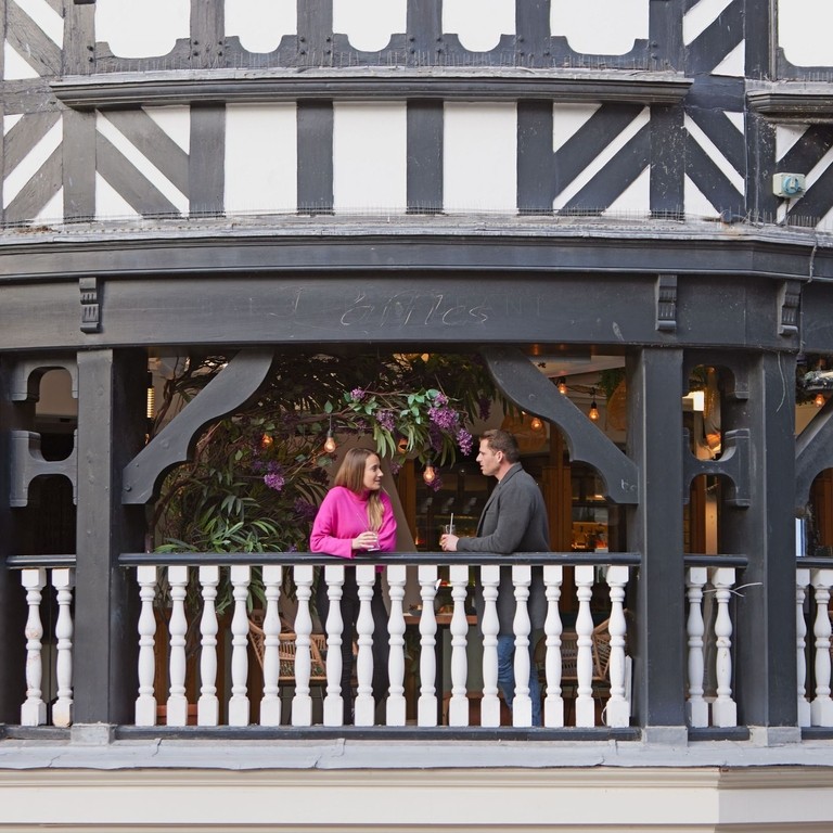 A man and a woman have a drink and talk on the balcony at a local cafe.
