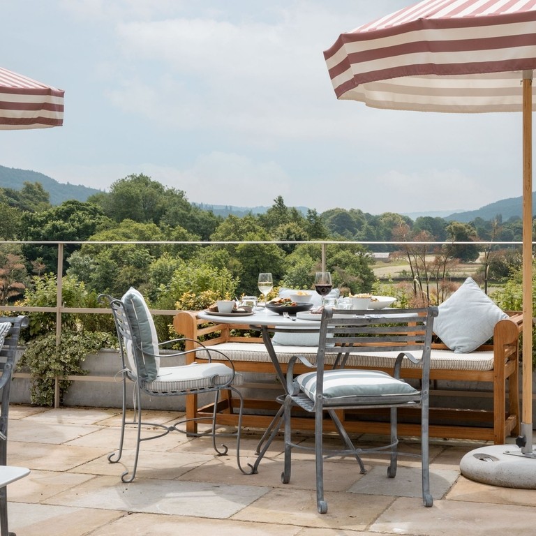 Tables on the patio with striped umbrellas overlooking the view at a luxury hotel on the grounds of a large country estate.