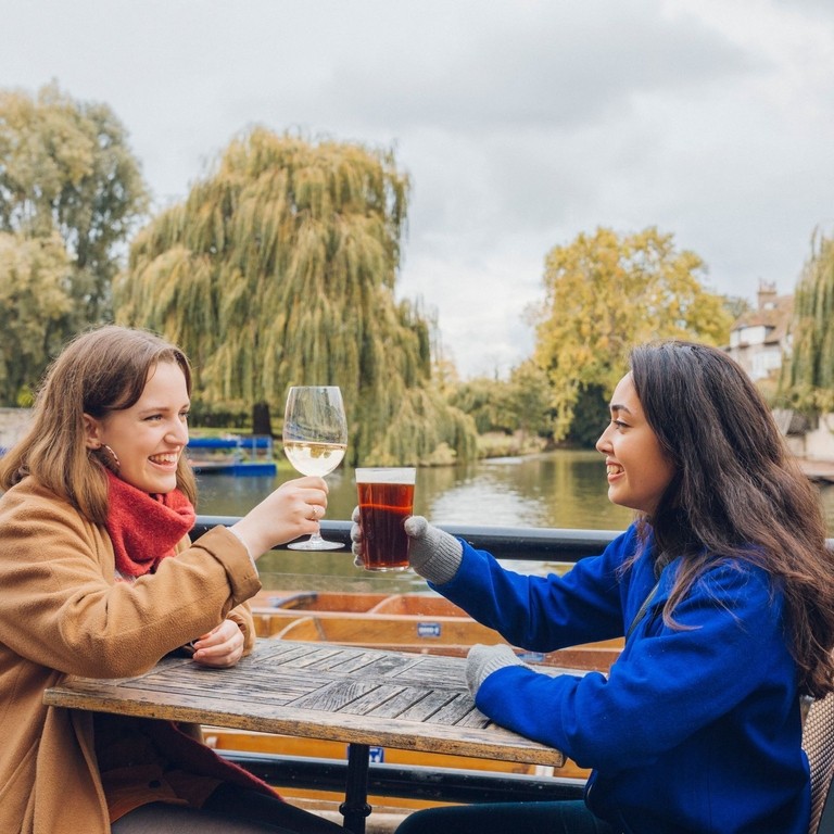 Two women toasting each other at a pub beside the river