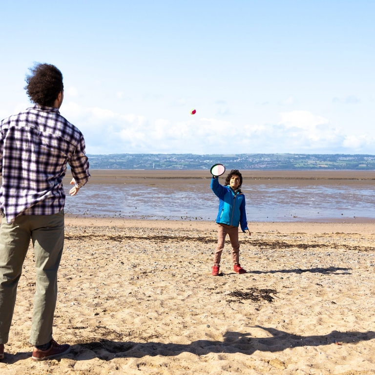 A man and a boy play a ball game on a beach