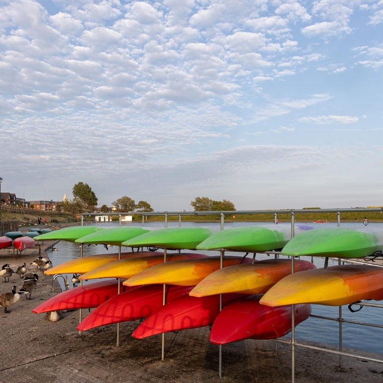 Multi coloured kayaks stacked on the shore with geese in the background