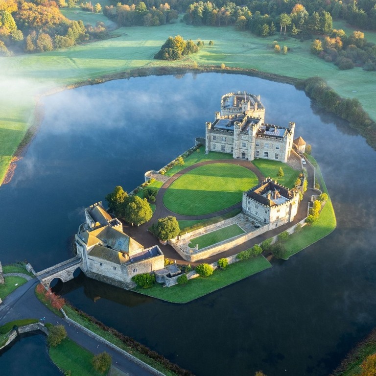 Aerial view of castle surrounded by a moat, river and trees during sunrise