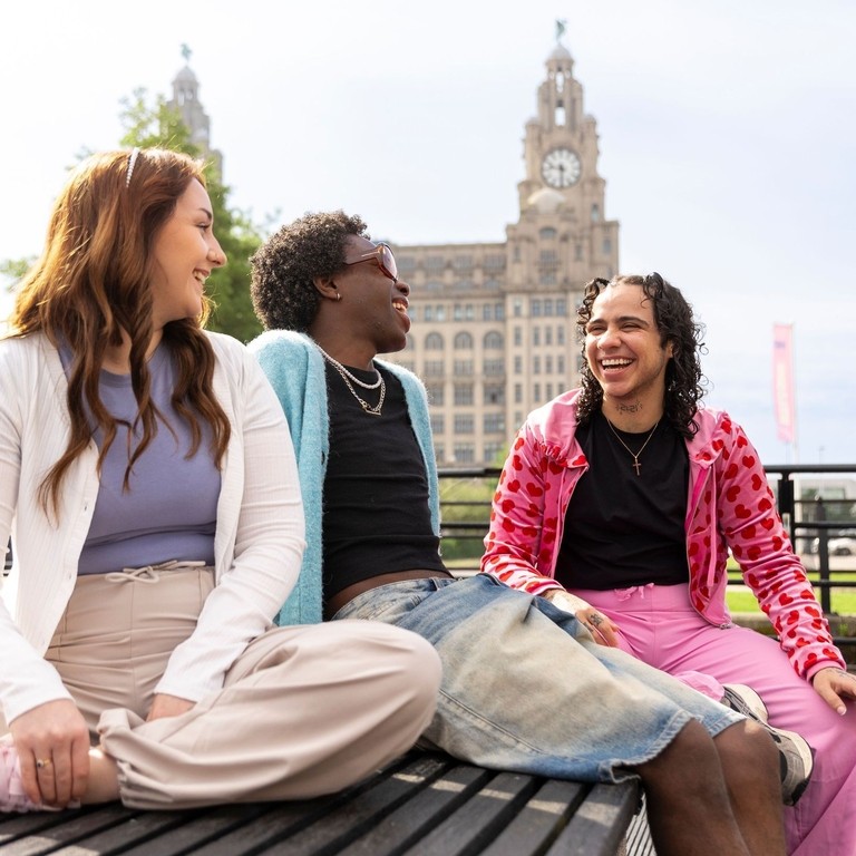 A group of friends sit together on a bench in front of an iconic building