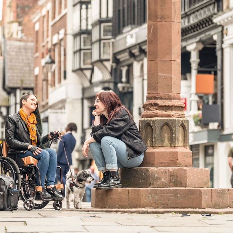 Two women sit talking together in a town centre