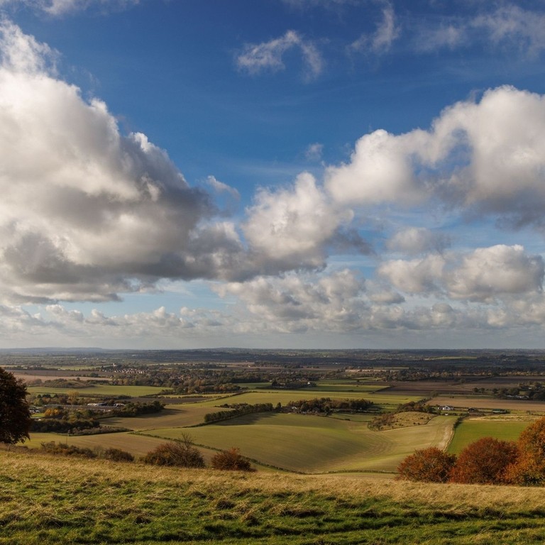 Panoramic view or rolling green farmland and pastures with a cloudy sky.