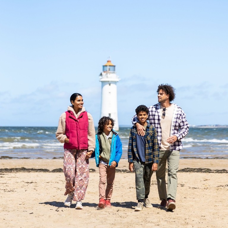 Family walk along a beach with a lighthouse in the background