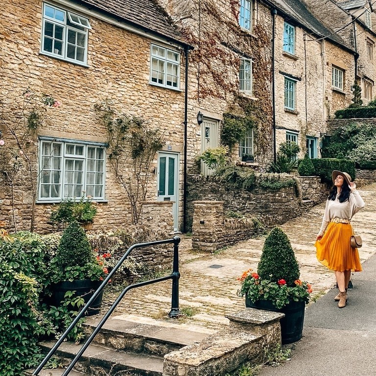 A woman in a hat walks down a street in a quaint village